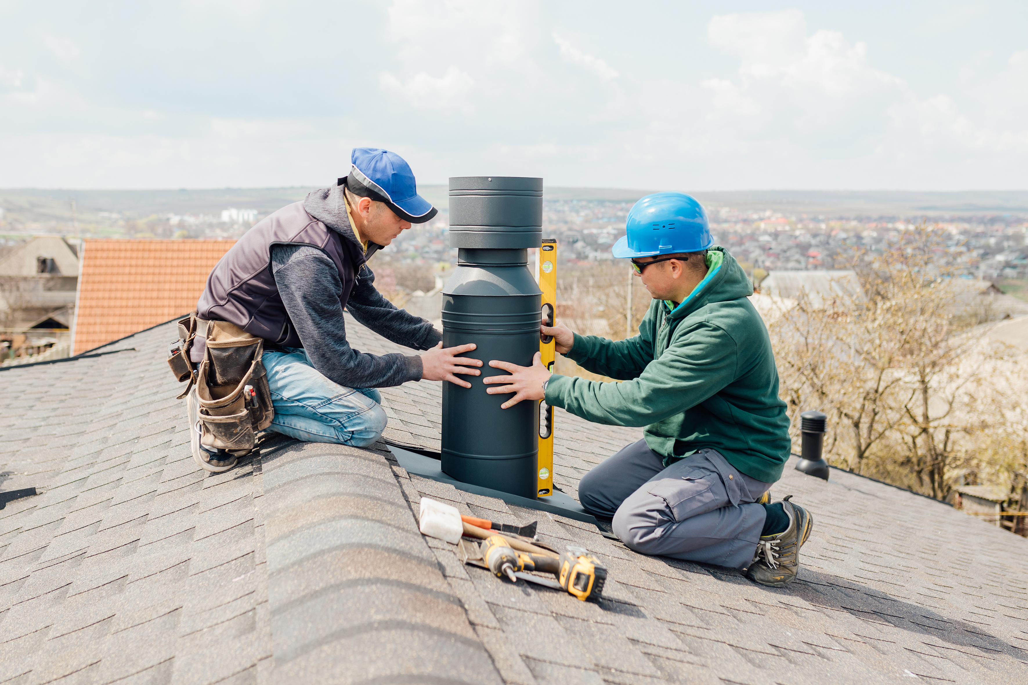 Workers on the roof installing tin cap on the iron chimney. roof